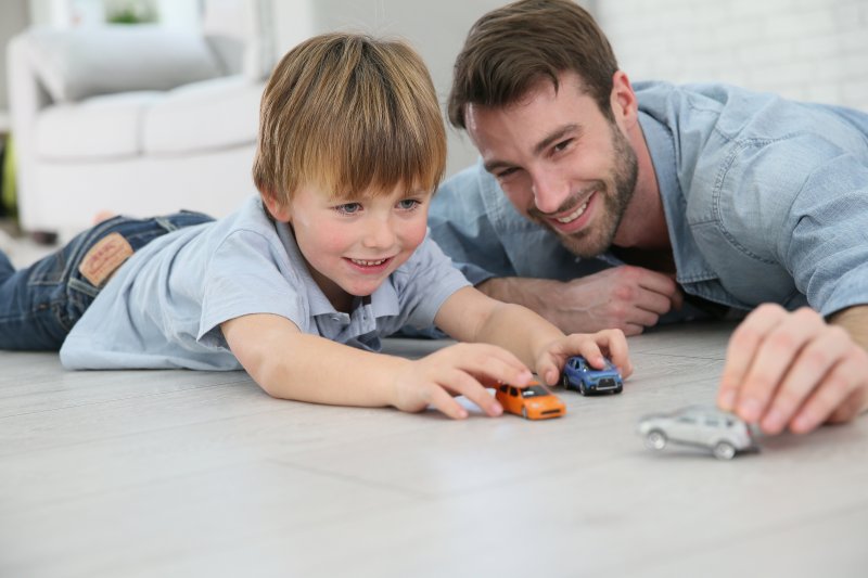 a father and his son playing with toy cars on the floor of their home